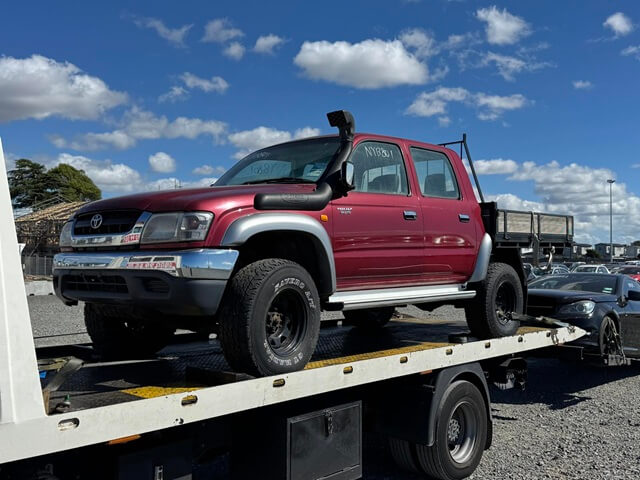 Red Toyota Hilux ute loaded on a flatbed tow truck for removal